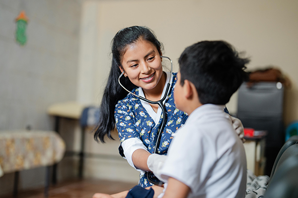 Verpleegkundige Marjorie uit Ecuador luistert met een stethoscoop naar de borst van een jongen.