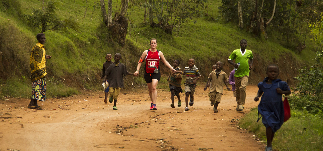 Een muskathleet rent samen met vrolijke kinderen op een zandweg in Rwanda.