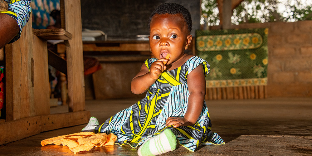 Baby Yawa uit Togo zit op de grond.