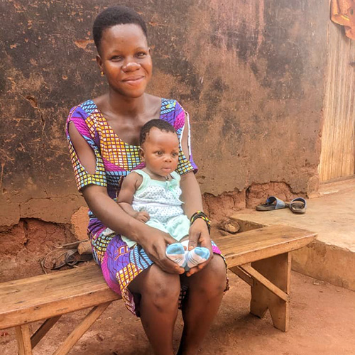 Davi uit Togo zit voor haar huis met baby Yawa op schoot. 