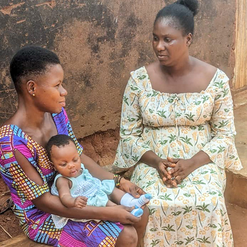 Davi uit Togo zit met een projectmedewerker en baby Yawa voor haar huis.