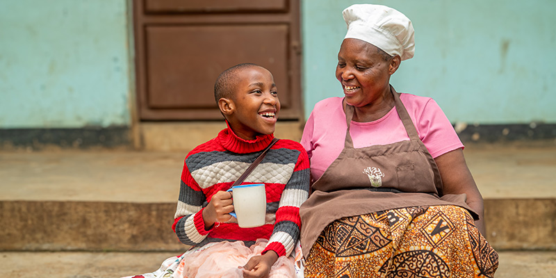 Kok Anna uit Tanzania zit naast een deelnemer van een Compassion-project.