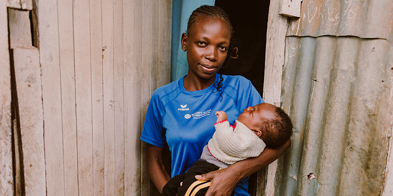 Moeder Juliet uit Kenia poseert met baby Jayson voor haar huis.