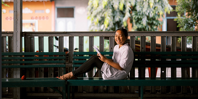 Vhio uit Indonesië zit op een bankje met een brief.