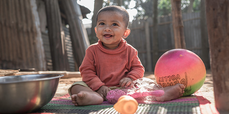 Baby Dhiraj uit Bangladesh met zijn speelgoed op een kleed buiten. 