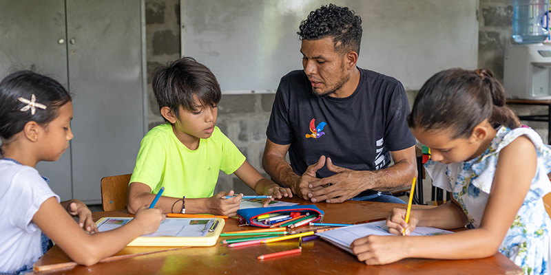 Kinderen uit Colombia zitten met hun begeleider aan tafel op het Compassion-project.