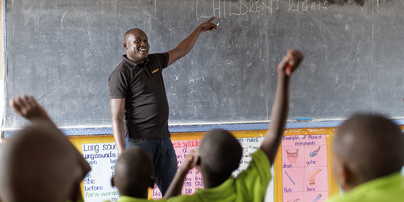 Projectmedewerker Moses uit Uganda staat voor een schoolbord.