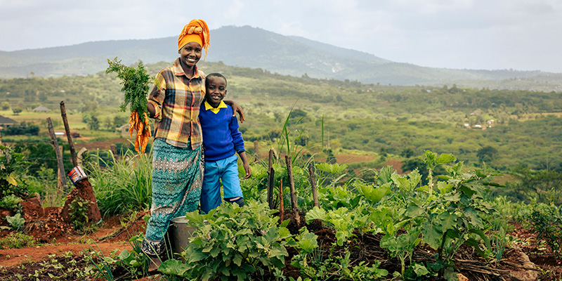Moeder Serah uit Kenia staat met zoon Junior in de moestuin.